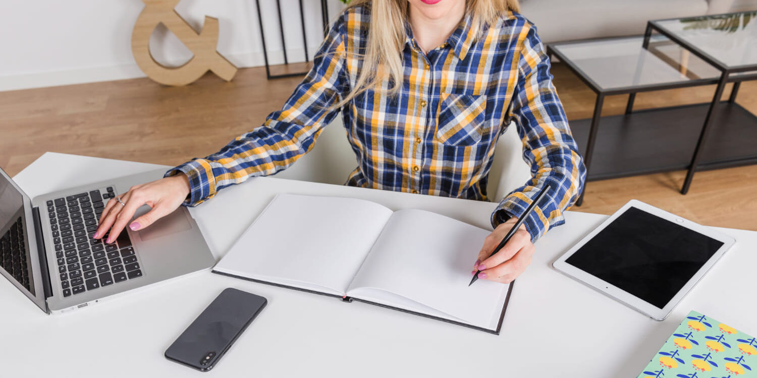 Freelancer werkt op laptop en maakt notities in schrift – zakelijke verzekeringen vergelijken