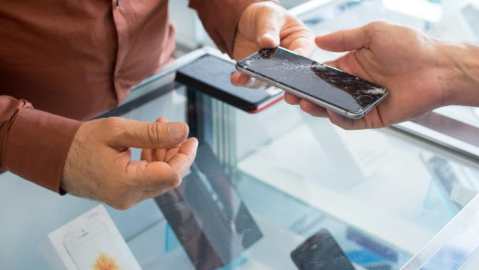 Overdracht van een smartphone met gebarsten scherm bij een telefoon reparatiepunt, klant en medewerker aan balie