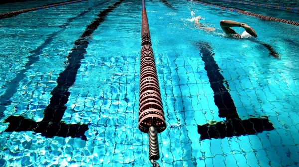 Zwemmer trekt baantjes in helderblauw buitenzwembad met duidelijke zwarte zwembaanlijnen