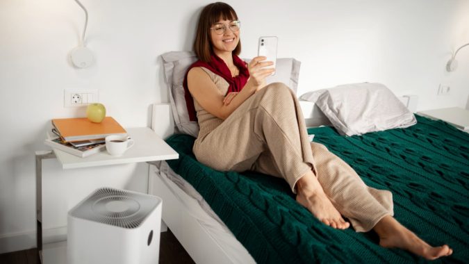 Vrouw zit ontspannen op bed met een Helthome luchtontvochtiger naast haar in de slaapkamer