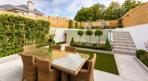 Moderne tuin met glazen tafel, rieten stoelen, gesnoeide bomen en strakke niveaus in een stadstuinontwerp