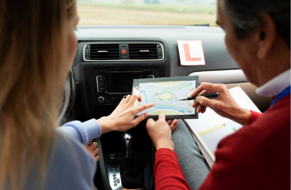 Rijinstructeur geeft aanwijzingen in de lesauto over een rotonde aan zijn leerling.